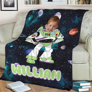 May include: A personalized blanket featuring a child's face superimposed on a Buzz Lightyear character design. The blanket has a dark blue space-themed background with planets and stars. The name "WILLIAM" is written in large, green letters.