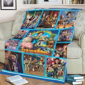 Puede incluir: Una manta azul y blanca con un collage de im&aacute;genes de la pel&iacute;cula animada Toy Story. La manta tiene un borde azul e incluye el texto "CUSTOM NAME". La manta est&aacute; sobre un sof&aacute; beige.