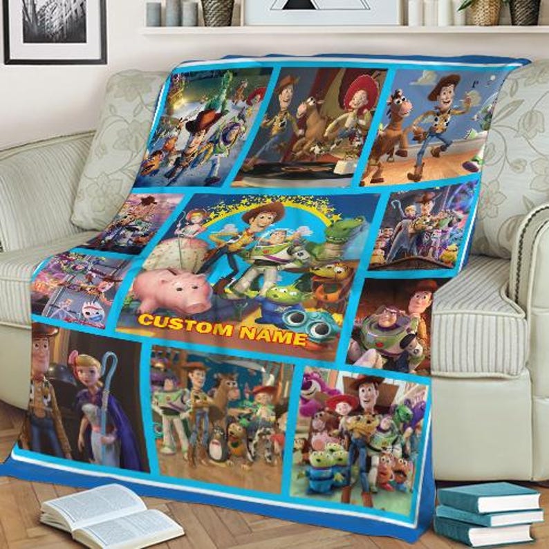Puede incluir: Una manta azul y blanca con un collage de im&aacute;genes de la pel&iacute;cula animada Toy Story. La manta tiene un borde azul e incluye el texto "CUSTOM NAME". La manta est&aacute; sobre un sof&aacute; beige.