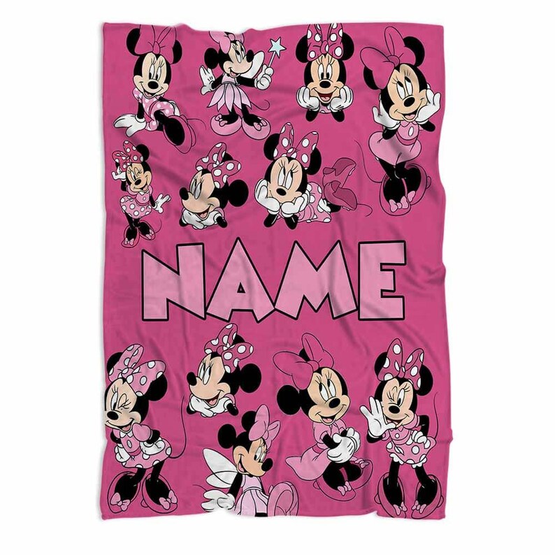 May include: A pink blanket featuring multiple illustrations of Minnie Mouse in various poses. The blanket has the word "NAME" in large pink letters across the center. Minnie Mouse is wearing pink dresses and bows with white polka dots.