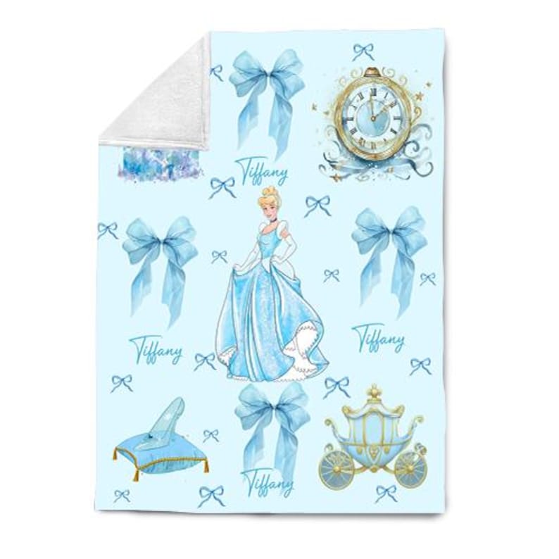 K&ouml;nnte beinhalten: Eine hellblaue Decke mit einem Aquarelldesign mit Aschenputtel, Schleifen, einer Kutsche, einer Uhr und einem Glasschuh. Der Name "Tiffany" ist kursiv geschrieben. Die Decke hat eine wei&szlig;e, flauschige R&uuml;ckseite.