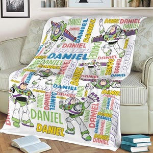 May include: White blanket featuring multiple images of Buzz Lightyear in various poses, with the name "DANIEL" repeated in colorful text. The blanket is draped over a sofa.