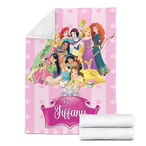 May include: Pink blanket featuring a group of cartoon princesses, with a pink and white striped background and crown accents. The name "Tiffany" is displayed in a pink banner. Two folded white towels are at the bottom.