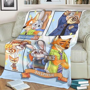 Pode incluir: Um cobertor com tema Zootopia com personagens de desenhos animados em estilo de hist&oacute;ria em quadrinhos. O cobertor tem um fundo azul claro com imagens de Judy Hopps, Nick Wilde e outros personagens. O nome "Jasmine" est&aacute; em uma faixa na parte inferior.