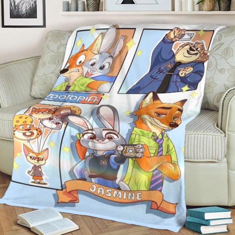 Pode incluir: Um cobertor com tema Zootopia com personagens de desenhos animados em estilo de hist&oacute;ria em quadrinhos. O cobertor tem um fundo azul claro com imagens de Judy Hopps, Nick Wilde e outros personagens. O nome "Jasmine" est&aacute; em uma faixa na parte inferior.