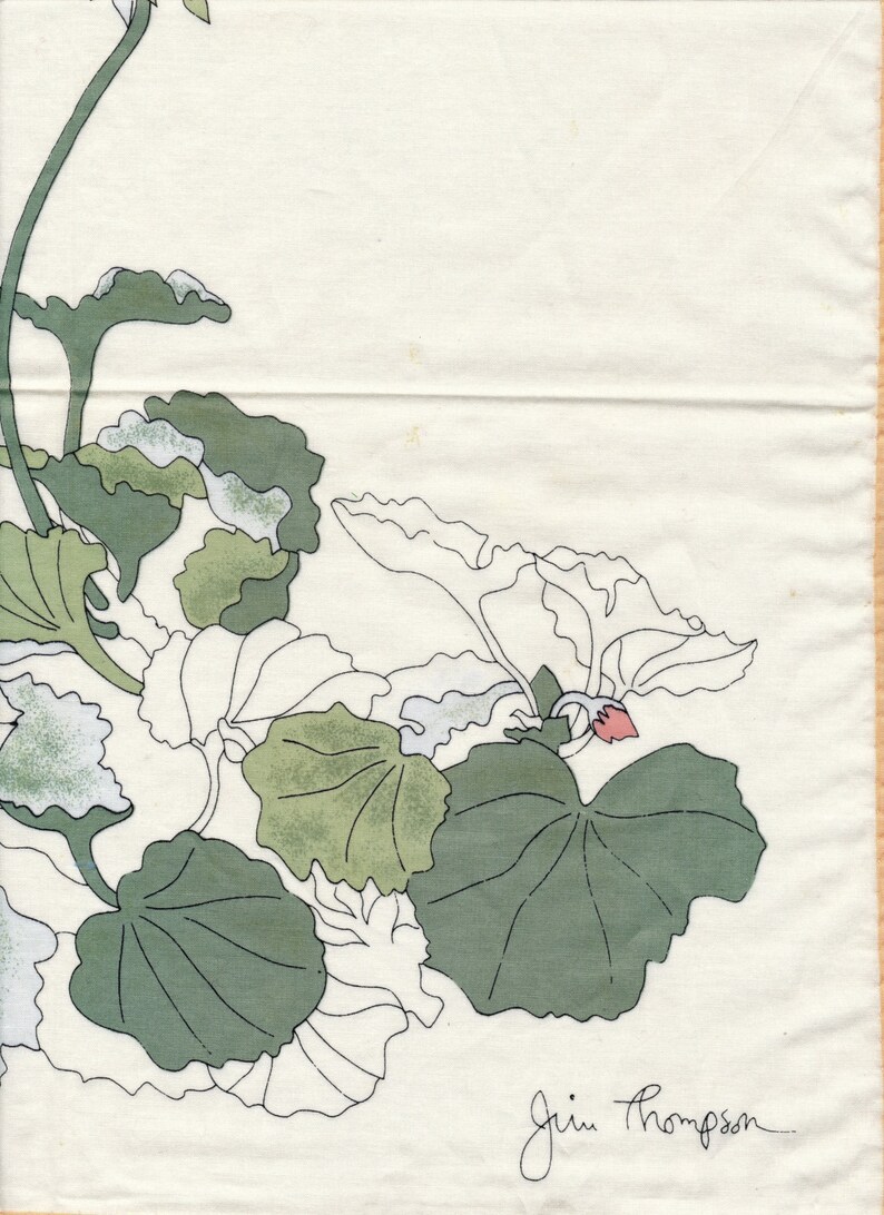 May include: Off-white fabric with a botanical design featuring green and white leaves and stems. A small pink flower is visible. The signature "Jim Thompson" is in the bottom right corner. The design is reminiscent of a vintage textile.