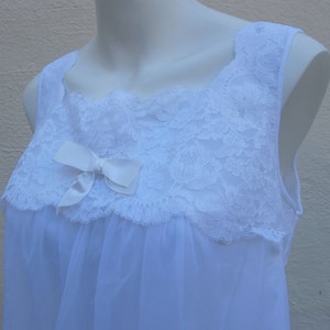 May include: White sleeveless nightgown with a square neckline. The bodice features a delicate lace overlay and a satin bow. The nightgown is made of a soft, flowing fabric.