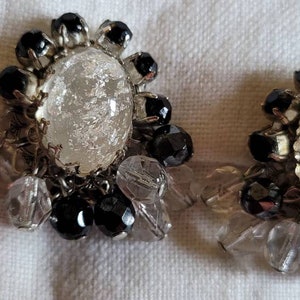 May include: A pair of clip-on earrings with a large, clear, faceted glass stone surrounded by black beads and smaller clear beads.