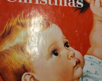 May include: A vintage children's book titled "Baby's Christmas" with a red cover. The cover features an illustration of a baby looking up at a Christmas ornament. The baby has blonde hair and is wearing a white and blue dress.