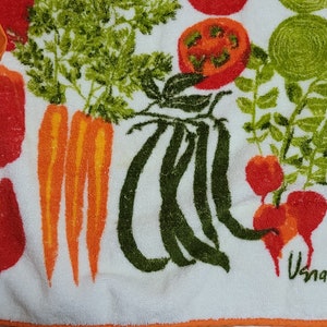 K&ouml;nnte beinhalten: Wei&szlig;es K&uuml;chentuch mit orangefarbenem Rand und einem bunten Gem&uuml;seprint. Der Druck zeigt Karotten, Paprika, Tomaten, gr&uuml;ne Bohnen und Radieschen. Das Handtuch hat das Wort "Usna" in der unteren rechten Ecke gedruckt.