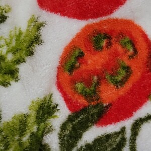 K&ouml;nnte beinhalten: Nahaufnahme eines wei&szlig;en Stoffes mit einer roten Tomate und gr&uuml;nen Blattmotiven. Die Tomate ist flauschig und hat eine rote und orange Farbe.