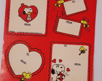 May include: Four red Valentine's Day gift tags featuring Snoopy and Woodstock. Each tag has a heart shape, a space for "To:" and "From:" and a copyright notice. The tags are printed on white paper with black outlines.