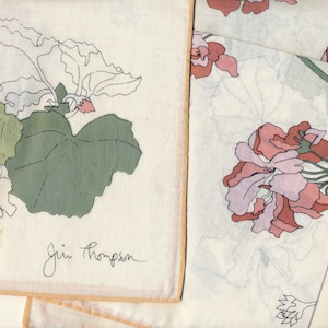 May include: Off-white handkerchiefs with floral designs. One handkerchief features green and white leaves with a small pink flower. Another handkerchief displays pink and lavender flowers. The Jim Thompson signature is visible on one handkerchief.