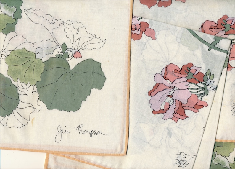 May include: Off-white handkerchiefs with floral designs. One handkerchief features green and white leaves with a small pink flower. Another handkerchief displays pink and lavender flowers. The Jim Thompson signature is visible on one handkerchief.