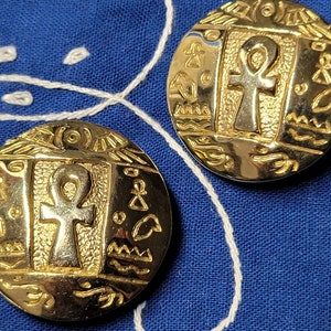 May include: A pair of gold-tone earrings with an ankh symbol and Egyptian-inspired designs.