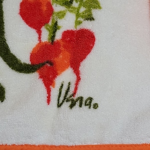 K&ouml;nnte beinhalten: Wei&szlig;es K&uuml;chentuch mit orangefarbenem Rand. Das Tuch zeigt eine gr&uuml;ne, bl&auml;ttrige Ranken mit roten und orangefarbenen Radieschen. Das Tuch ist mit "Vinga." signiert.