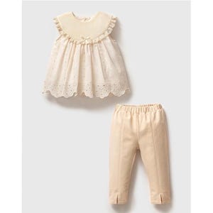 May include: A two-piece outfit for a baby or toddler, featuring a white eyelet top with a scalloped hem and a pair of beige pants.