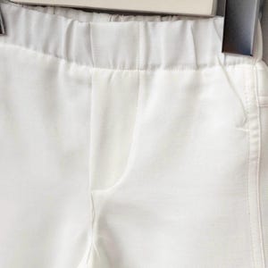 K&ouml;nnte beinhalten: Nahaufnahme einer wei&szlig;en Hose mit elastischem Bund und einer Taschennaht. Der Stoff scheint ein glattes, gewebtes Material zu sein. Die Hose h&auml;ngt an einem Kleiderb&uuml;gel.