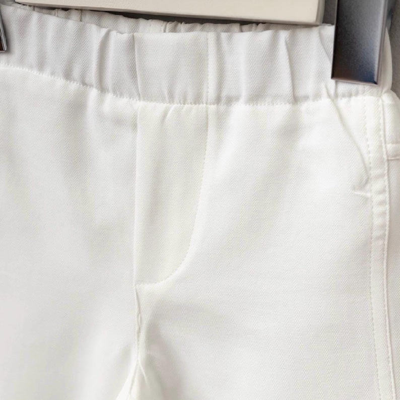 K&ouml;nnte beinhalten: Nahaufnahme einer wei&szlig;en Hose mit elastischem Bund und einer Taschennaht. Der Stoff scheint ein glattes, gewebtes Material zu sein. Die Hose h&auml;ngt an einem Kleiderb&uuml;gel.