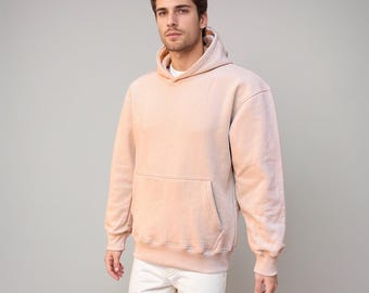 May include: A light pink hooded sweatshirt with a kangaroo pocket. The sweatshirt has a relaxed fit and a slightly faded look.