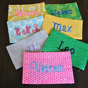May include: Six personalized fabric pouches with different patterns and names embroidered on them. The names are: Sloane, E & M L, Allie, Max, Leo, and Victoria.