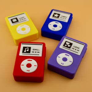 Pode incluir: Quatro leitores de MP3 de brinquedo coloridos em amarelo, azul, vermelho e roxo. Cada leitor tem um ecrã branco com ícones e texto, e um painel de controlo circular branco. O leitor amarelo diz "LUCK", o azul "VIBES", o vermelho "CHILL" e o roxo "LOVE".