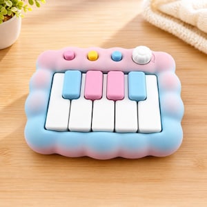 Op de afbeelding: Een speelgoedpiano in pastelkleuren met een wolkvormig frame. De piano heeft witte toetsen, met blauwe en roze toetsen ertussen. Het heeft roze, gele en blauwe knoppen en een witte knop. Het ontwerp is zacht en speels, geschikt voor kinderen.