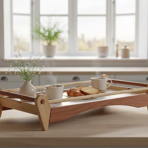 May include: A wooden serving tray with a light wood frame and a darker wood base. The tray holds two mugs, pastries, and a small vase of flowers. The tray is on a light-coloured countertop in a kitchen setting.