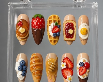 May include: A set of ten artificial nails, each adorned with miniature food designs. The nail art includes pancakes, a chocolate-covered strawberry, a waffle, toast with jam, a fried egg, whipped cream with blueberries, a croissant, honey, strawberries, and more.