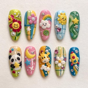May include: A set of ten artificial nails, each uniquely designed with colorful, whimsical 3D art. Designs include a smiling flower, a panda holding a star, a giraffe, a rainbow, and a rocket ship, among others. The nails are oval-shaped and feature a glossy finish.