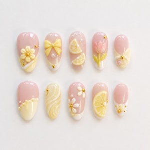 Pode incluir: Um conjunto de dez unhas artificiais com vários designs. As unhas apresentam uma base rosa claro, adornadas com flores amarelas, laços, fatias de limão e uma tulipa. Algumas unhas têm detalhes dourados e pontas brancas.
