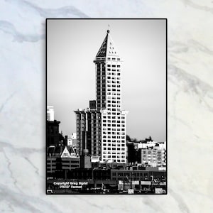 May include: A black and white photograph of the Space Needle in Seattle, Washington. The iconic skyscraper is seen against a cloudy sky with other buildings in the background.
