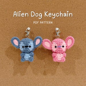 May include: Two handmade crochet Alien Dog keychains, one blue and one pink, with large ears and black eyes. The keychains are attached to silver clasps. Text on the image reads "Alien Dog Keychain" and "PDF Pattern."