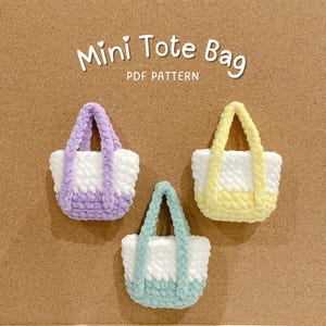 May include: Three miniature crochet tote bags in pastel shades: lavender, yellow, and mint green. Each bag has a white body with a coloured base and handles. The text "Mini Tote Bag PDF Pattern" is at the top.