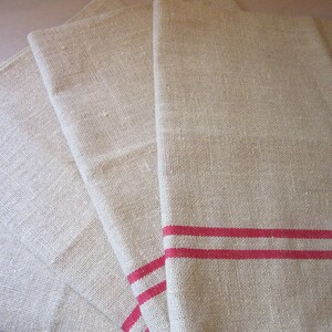 May include: Four natural linen tea towels, one with two red stripes. The towels are folded and stacked on top of each other.