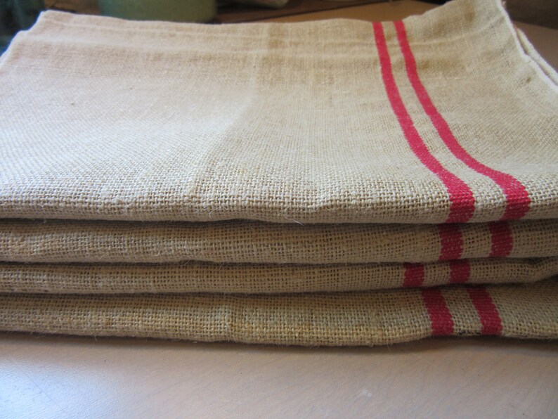 May include: A stack of four linen tea towels with red stripes. The towels are folded and have a rustic, farmhouse style.