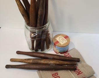 May include: A collection of vintage wooden rolling pins in a glass jar and scattered on a white surface. Several pins are displayed, with a cork-topped container and folded linen towels with red text reading "BON APP".