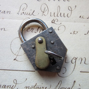 Puede incluir: Un candado hexagonal vintage con un pestillo de latón y una llave adjunta. El candado es de metal y tiene un aspecto desgastado y envejecido.