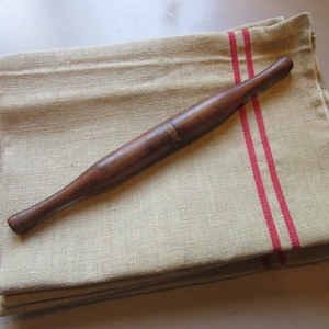 May include: A wooden rolling pin with a brass band lies on a folded linen kitchen towel with two red stripes.