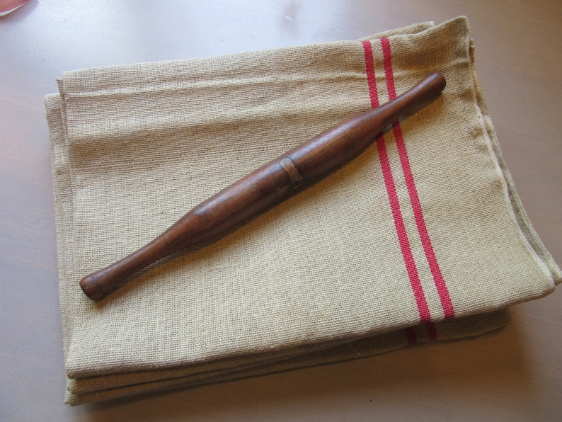 May include: A wooden rolling pin with a brass band lies on a folded linen kitchen towel with two red stripes.