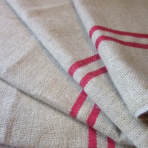 May include: A set of three linen tea towels with red stripes. The towels are folded and stacked on top of each other.