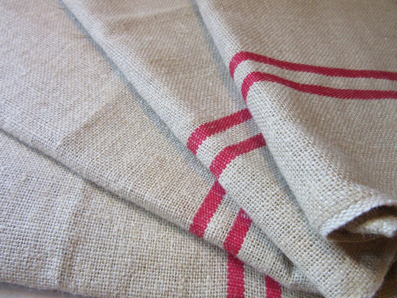 May include: A set of three linen tea towels with red stripes. The towels are folded and stacked on top of each other.