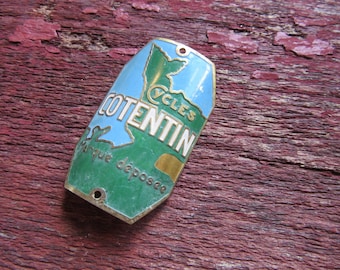 May include: A vintage bicycle badge with a green and blue map of a region, the text "CYCLES COTENTIN" in gold lettering, and the words "Marque deposee" in smaller lettering.