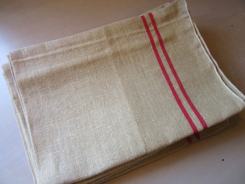May include: A stack of natural linen tea towels with two red stripes.