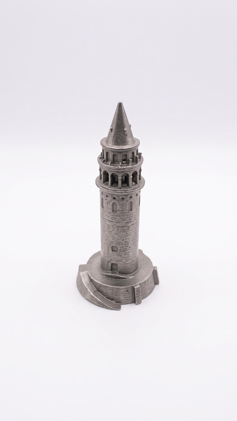 Raw finish Galata Tower miniature in unpolished cast stainless steel seen from a slight angle, showing the round base and conical roof on a white background