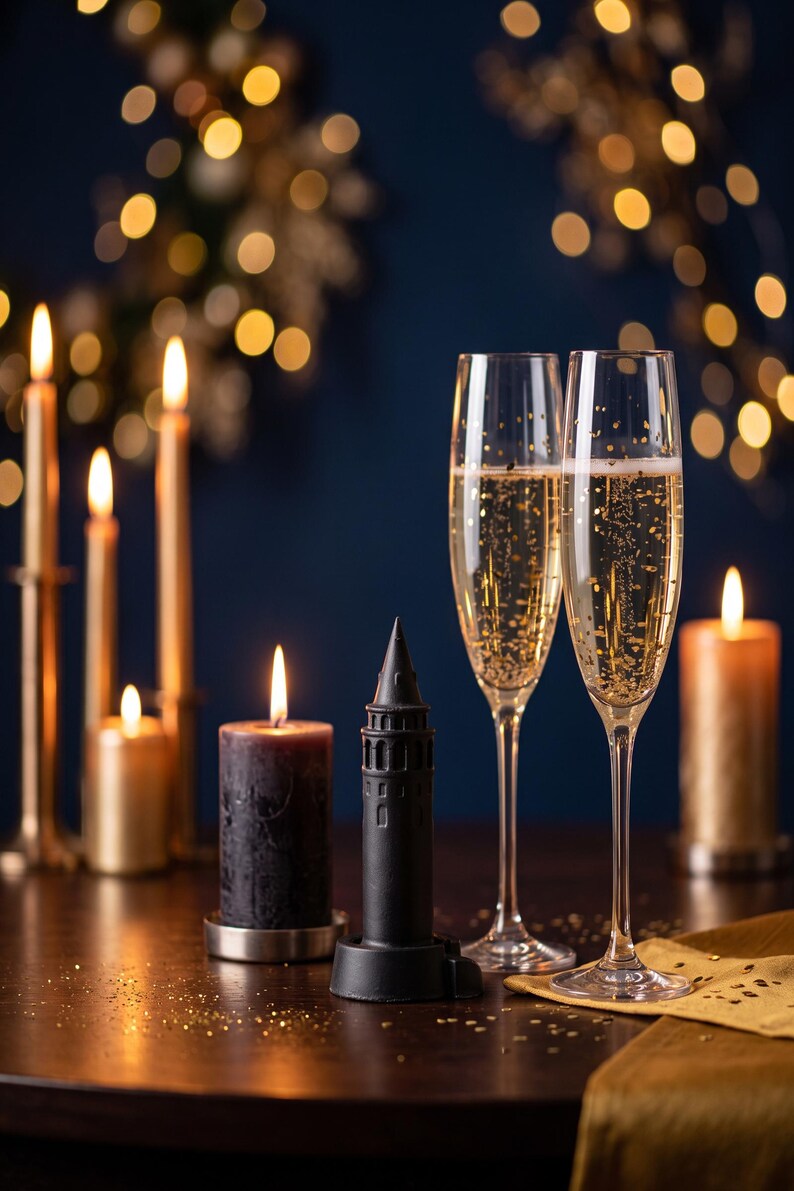 Black finish Galata Tower miniature beside champagne glasses and lit candles with gold lights on a navy background for New Year's Eve