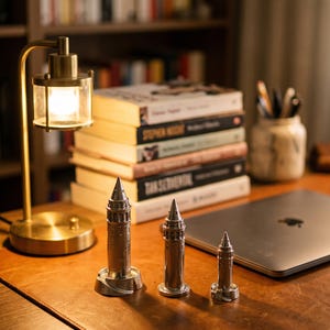 Three Galata Tower miniatures on a wooden desk beside a small brass lamp, a stack of books and a laptop