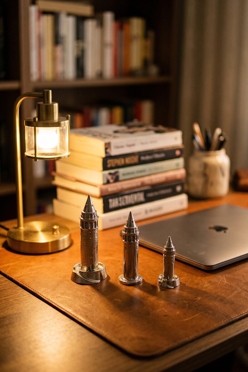 Three Galata Tower miniatures on a wooden desk beside a small brass lamp, a stack of books and a laptop