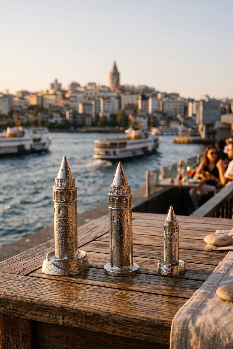 Three Galata Tower miniatures on a wooden terrace table with the Bosphorus and the Istanbul skyline behind them