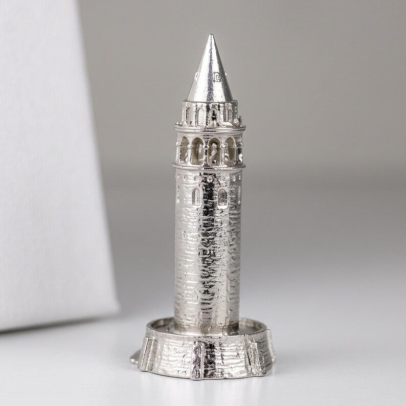 Polished stainless steel miniature of the Galata Tower on a round base against a light gray background